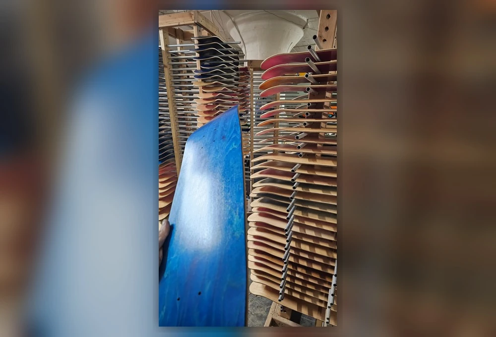 Zoomed-out view of a blue skateboard deck and racks of pressed decks inside Empire Skateboard Manufacturing